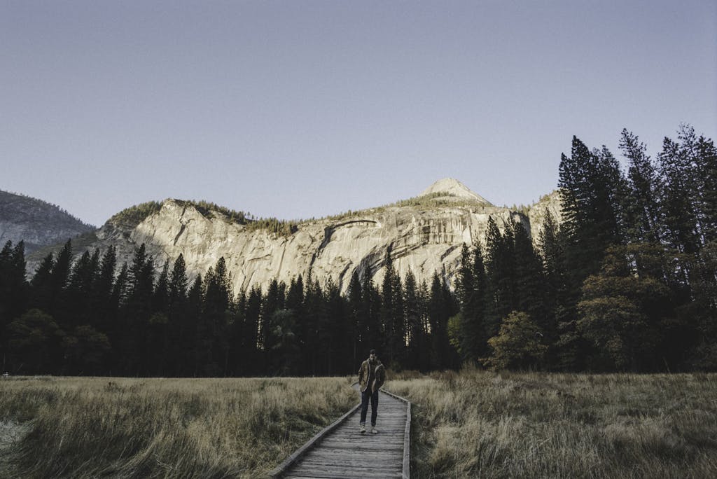A man walks alone on a wooden pathway in Yosemite Valley surrounded by mountains and trees.